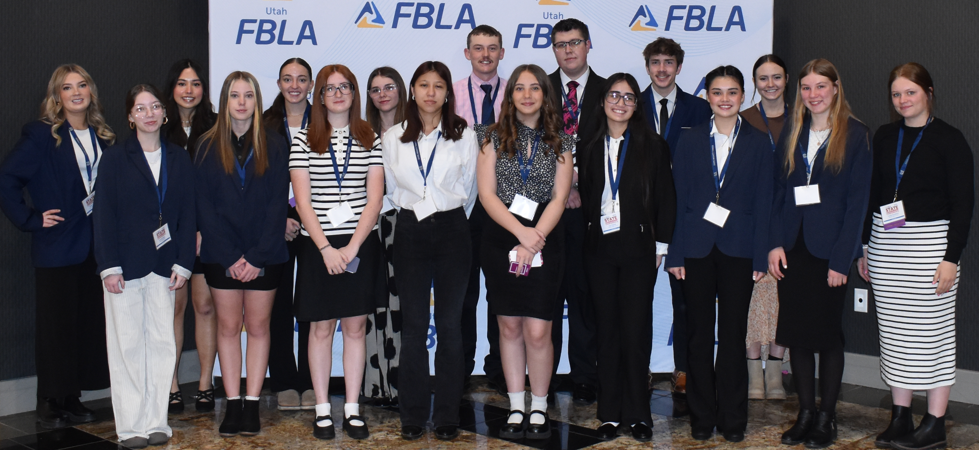 A large group of students in professional attire stand together for a photo in front of an FBLA backdrop.